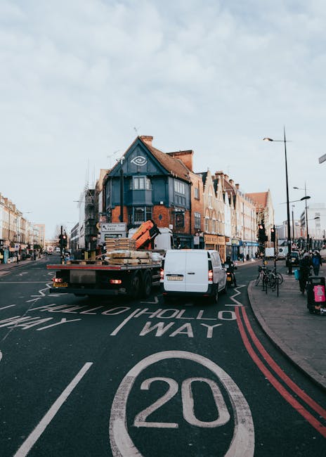 A red double-decker bus with route number 9 and destination 'Hammersmith' is driving along a busy city street in London, surrounded by pedestrians walking on the sidewalk and crossing the road. The st